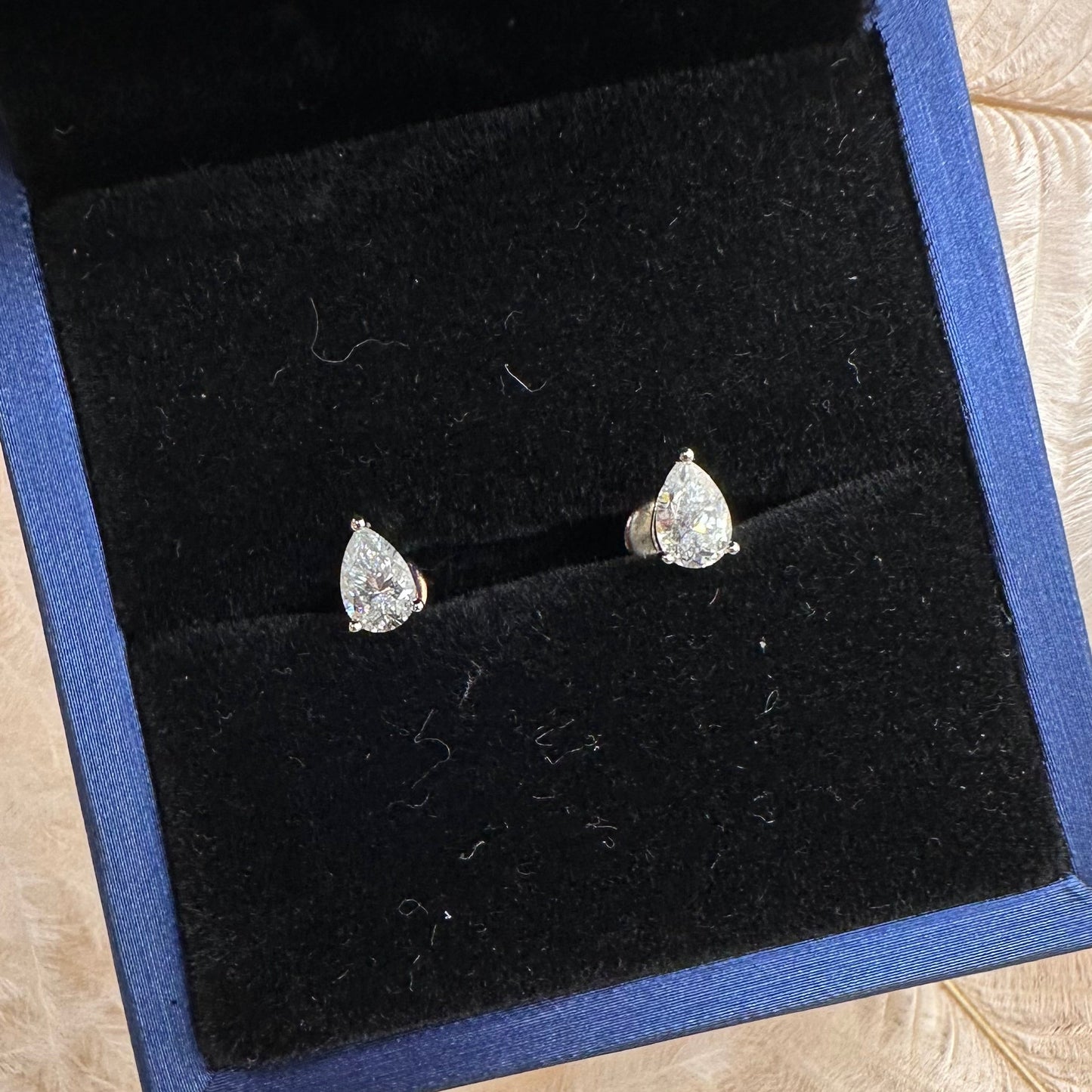Teardrop-shaped silver earrings in a black jewelry box on a beige surface