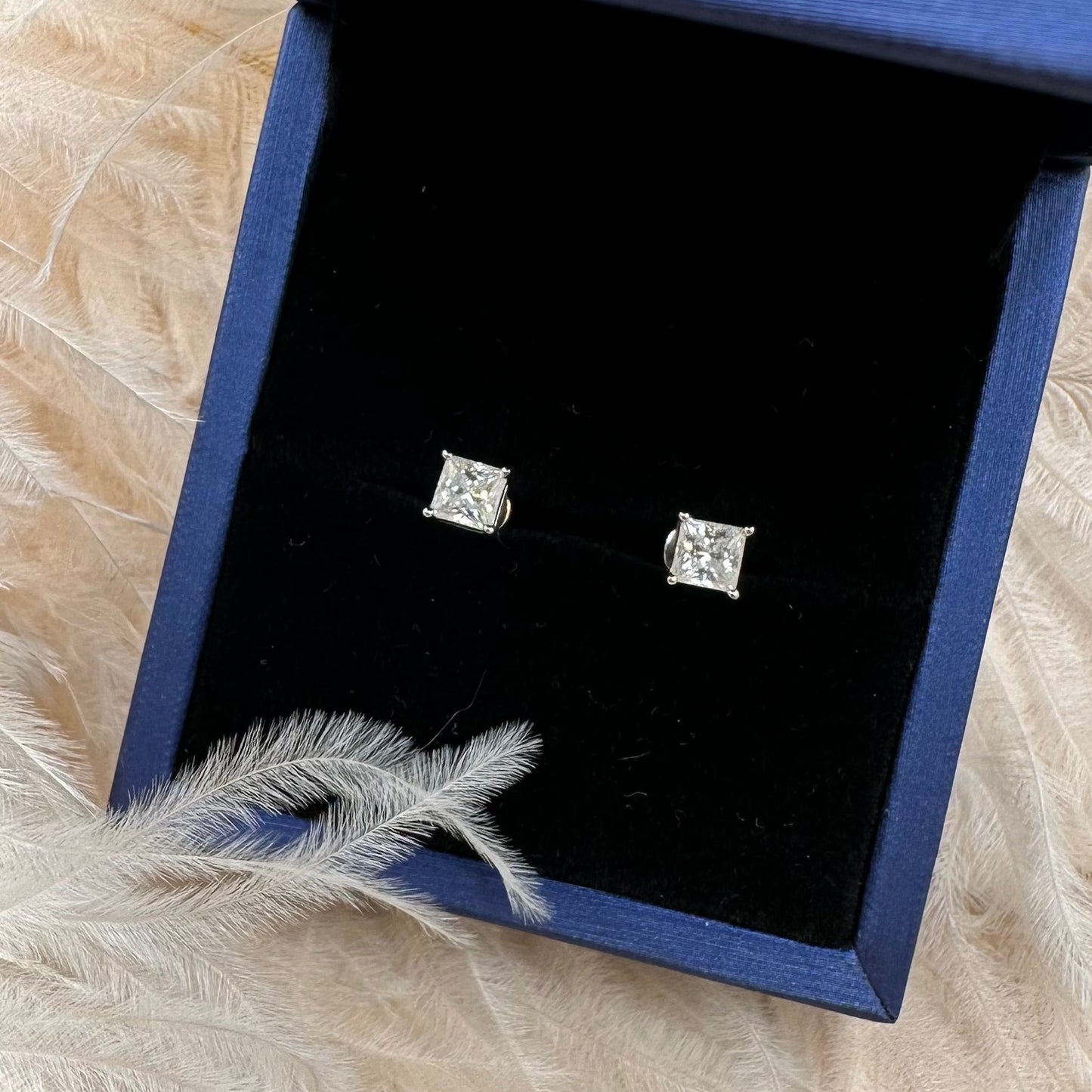 Pair of diamond stud earrings in a blue jewelry box on a fur surface